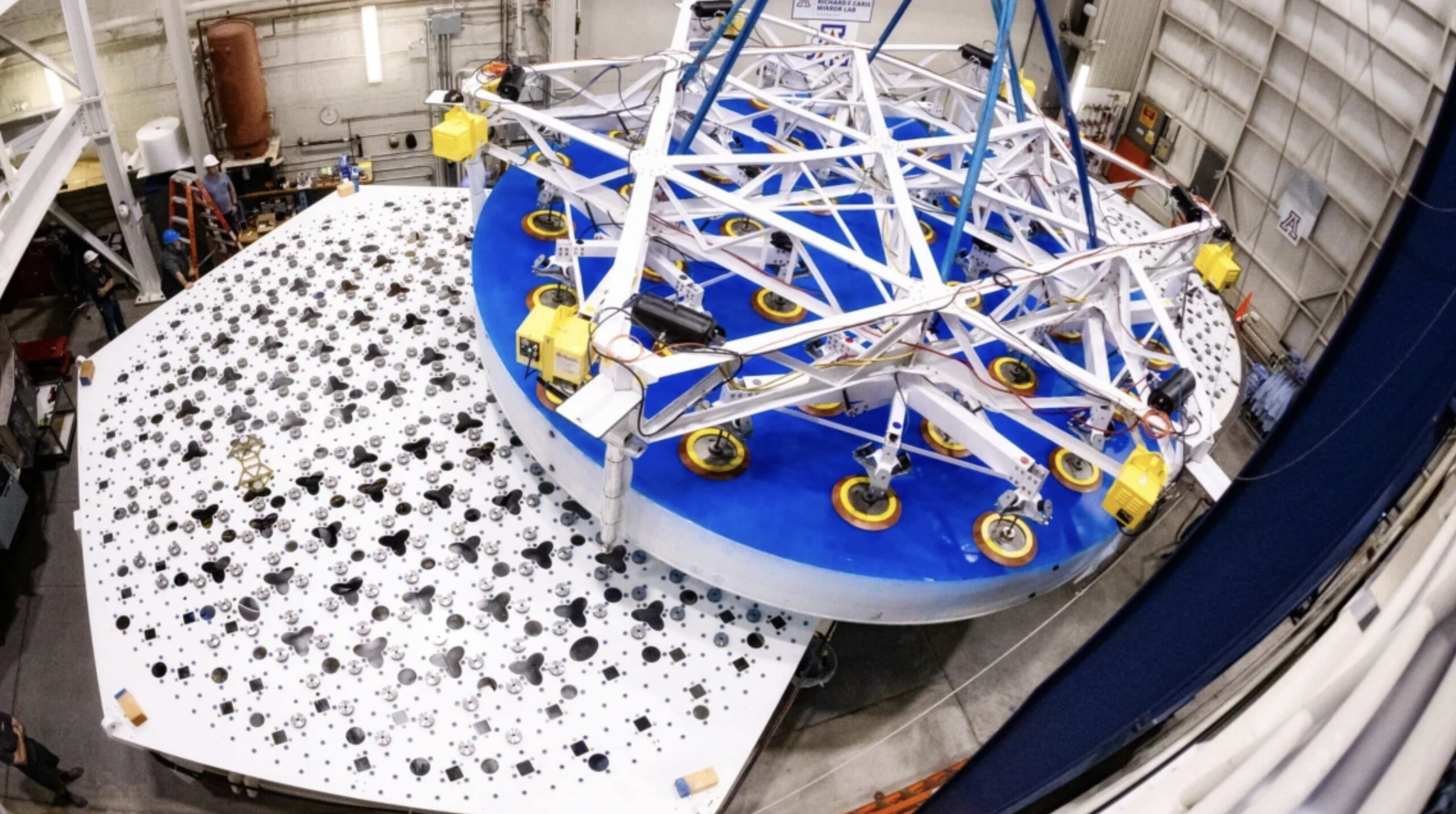 Suspended by suction cups, one of the Giant Magellan Telescope's seven primary mirror segments is hoisted onto its support structure by a crane at the Richard F. Caris Mirror Lab.